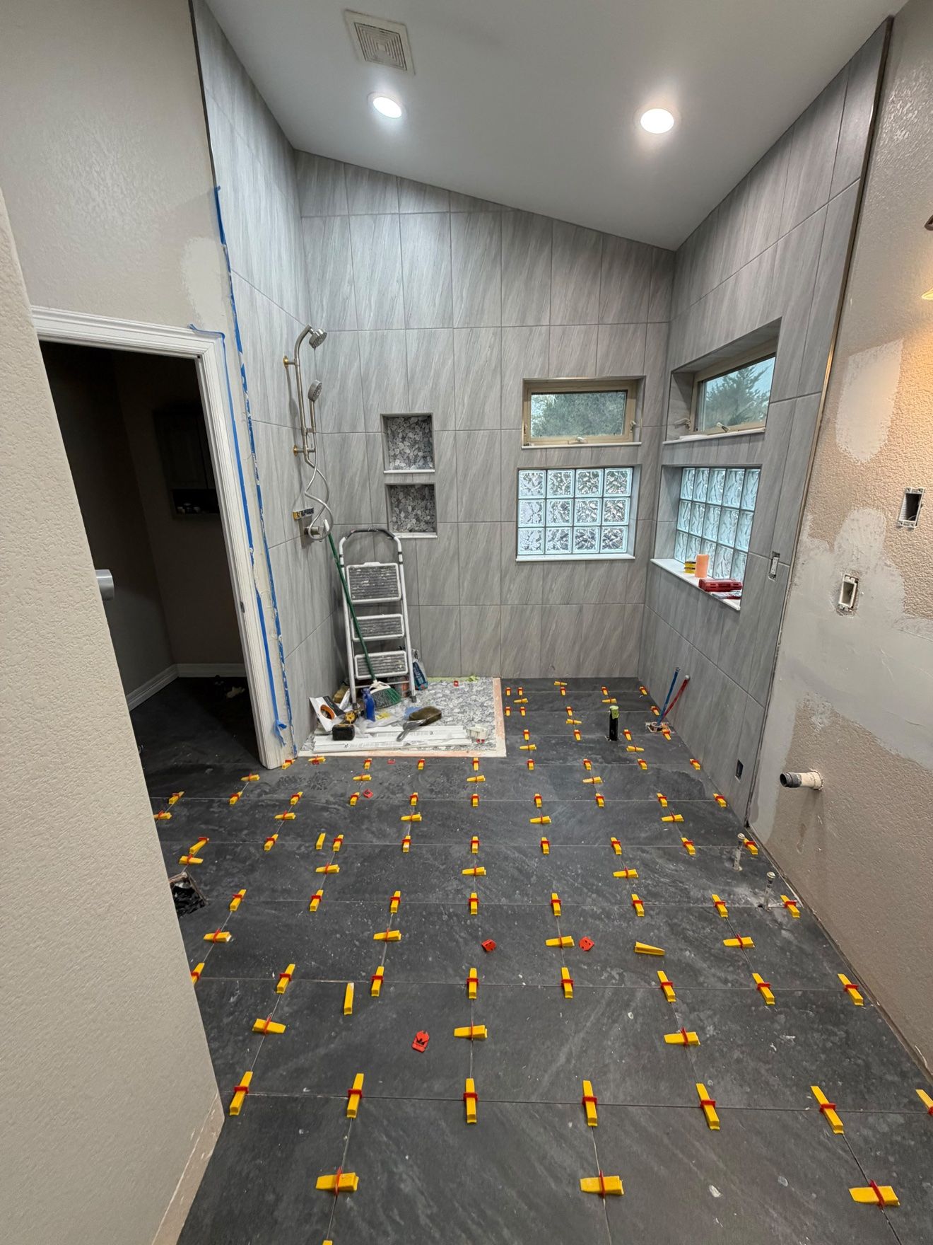Large-format bathroom tile being set with a leveling system